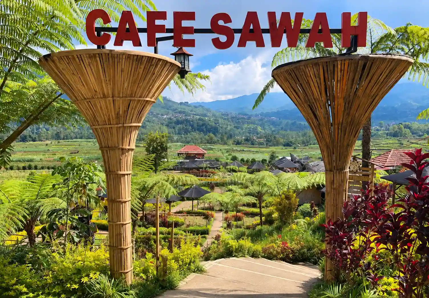 Gerbang bambu ikonik bertuliskan Cafe Sawah Pujon Kidul dengan latar sawah hijau dan pegunungan