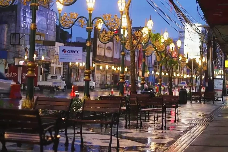 Koridor Kayutangan Heritage Malang saat sore dengan lampu gantung klasik menyala dan deretan bangku taman