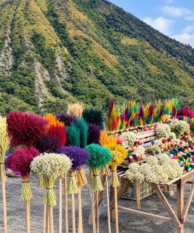 Lapak souvenir khas Bromo berisi rangkaian bunga edelweis dan kerajinan warna-warni dengan latar lereng Gunung Bromo